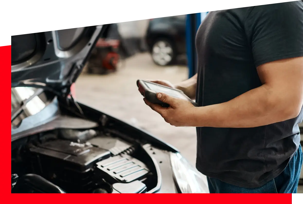 A man stands with a tablet in hand, inspecting a car engine, highlighting the intersection of technology and mechanics.