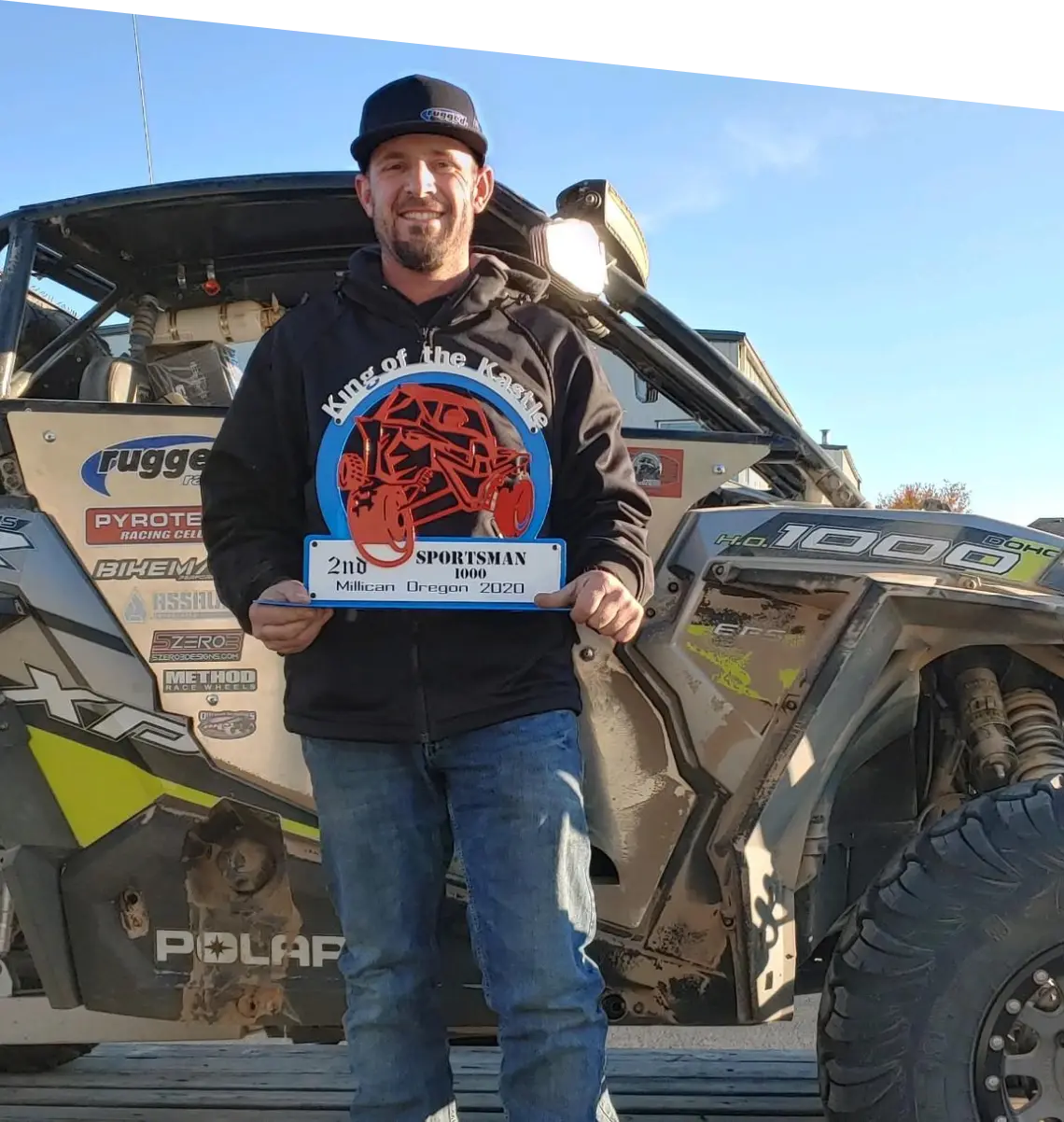 An irregular shaped photo of a man holding a plaque while standing next to a quad ATV in an outdoor setting.