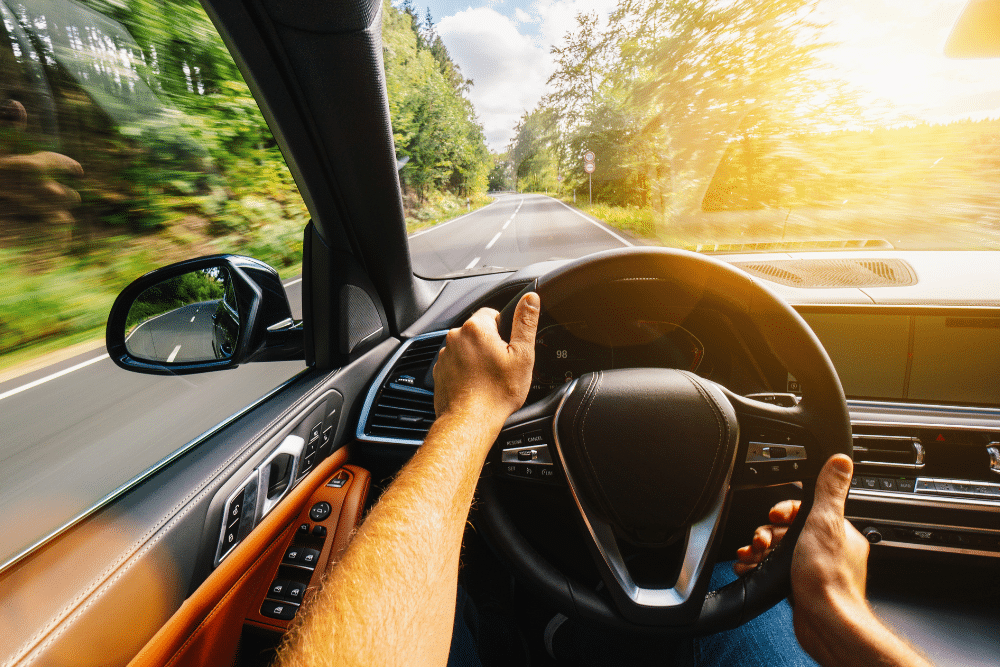summer driving, auto repair in Bend, OR at Mountain View Imports. POV of a driver in a modern car navigating a bright, sunlit road surrounded by trees, emphasizing smooth driving and vehicle control.