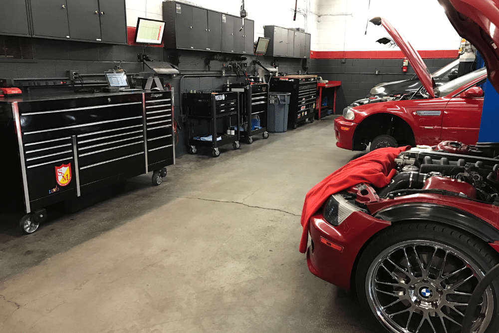 Car care, auto repair in Bend, OR at Mountain View Imports. Automotive repair shop interior with tool cabinets, diagnostic equipment, and two BMW cars with open hoods being serviced